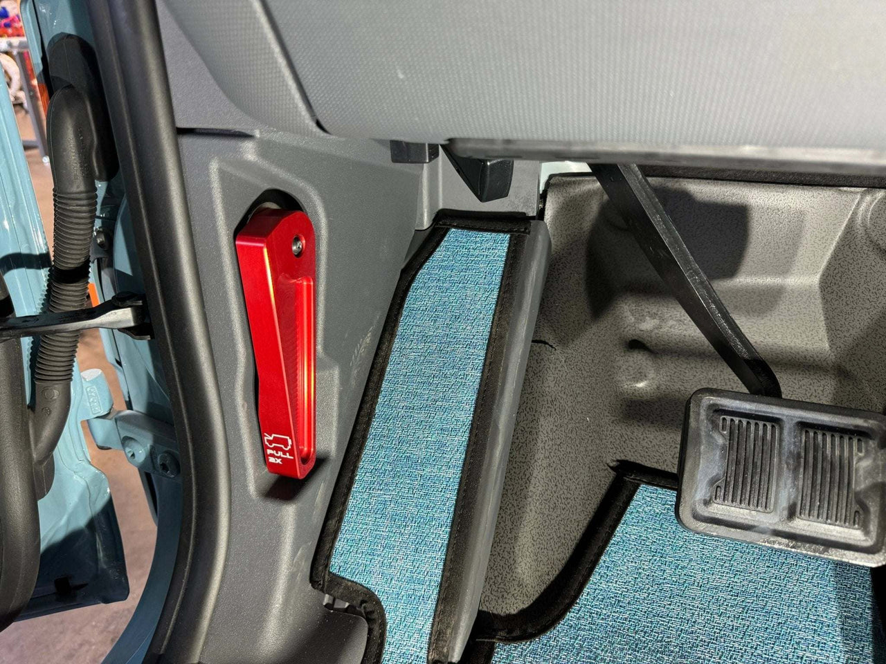 Red Grenadier Hood Release Handle installed on vehicle interior near driver's side pedals