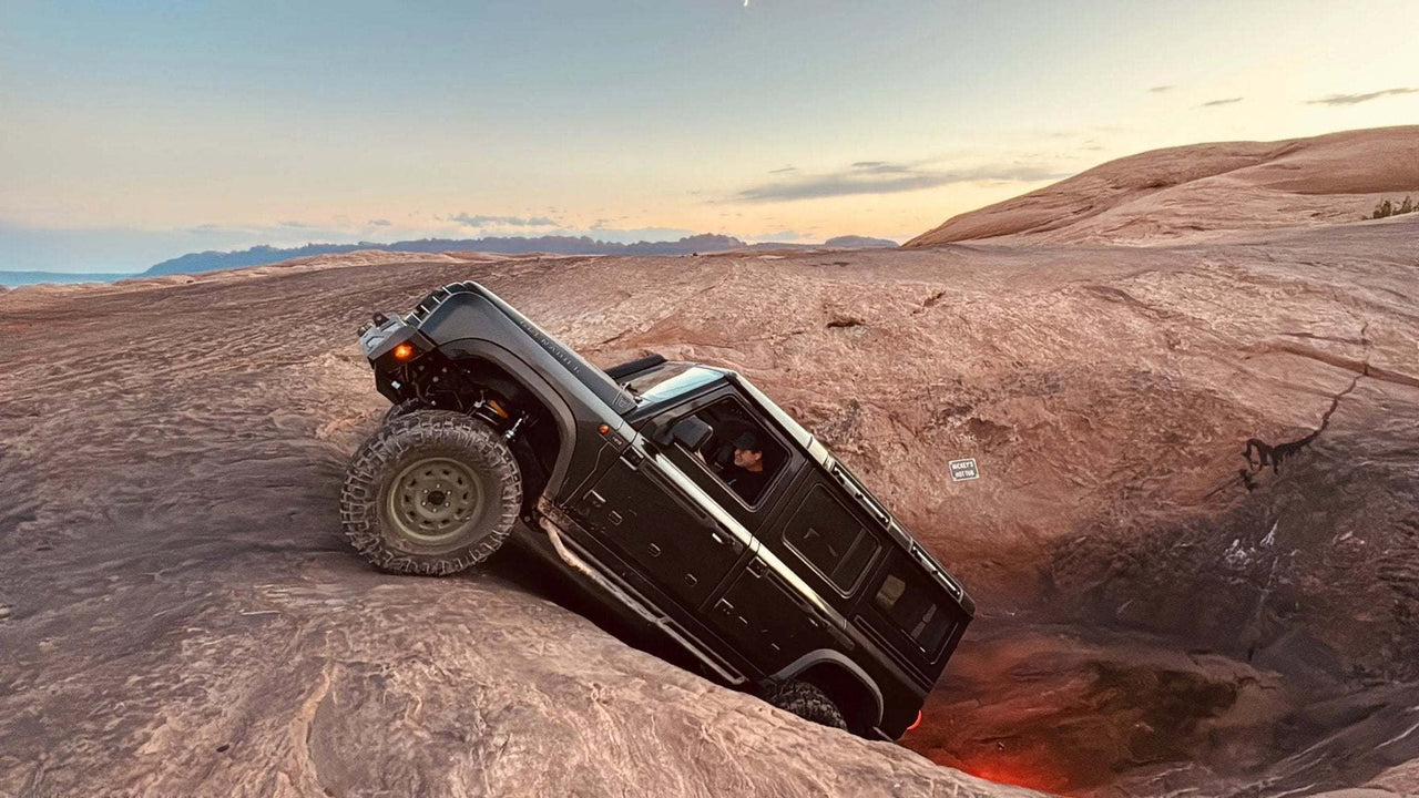 Off-road vehicle equipped with tubular Grenadier side steps and rock sliders climbing rocky terrain at sunset
