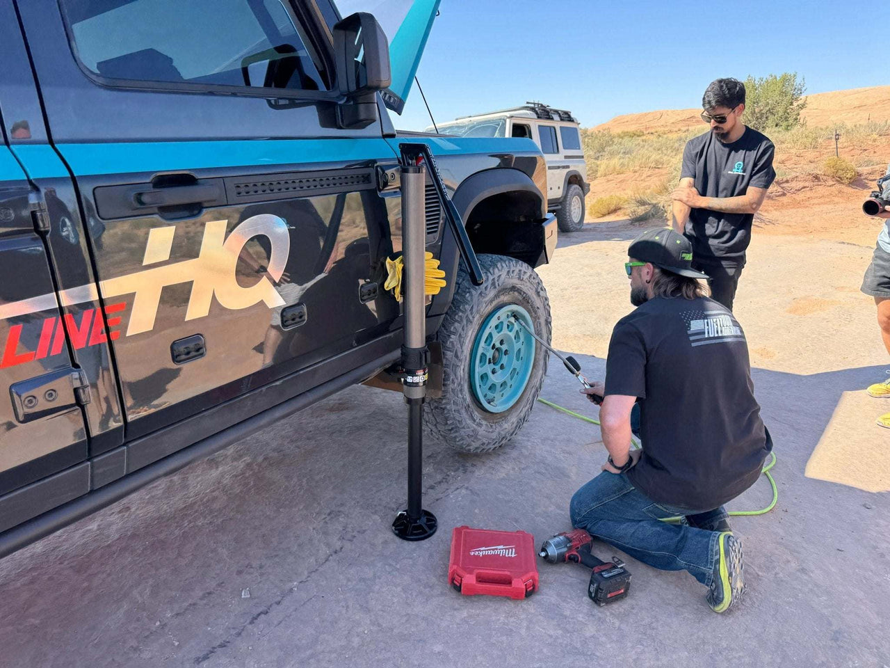 Black Grenadier side steps installed on off-road vehicle with people working on tire outdoors