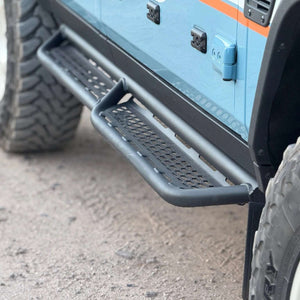 Close-up of tubular Grenadier side steps and rock sliders mounted on blue off-road vehicle with rugged tires