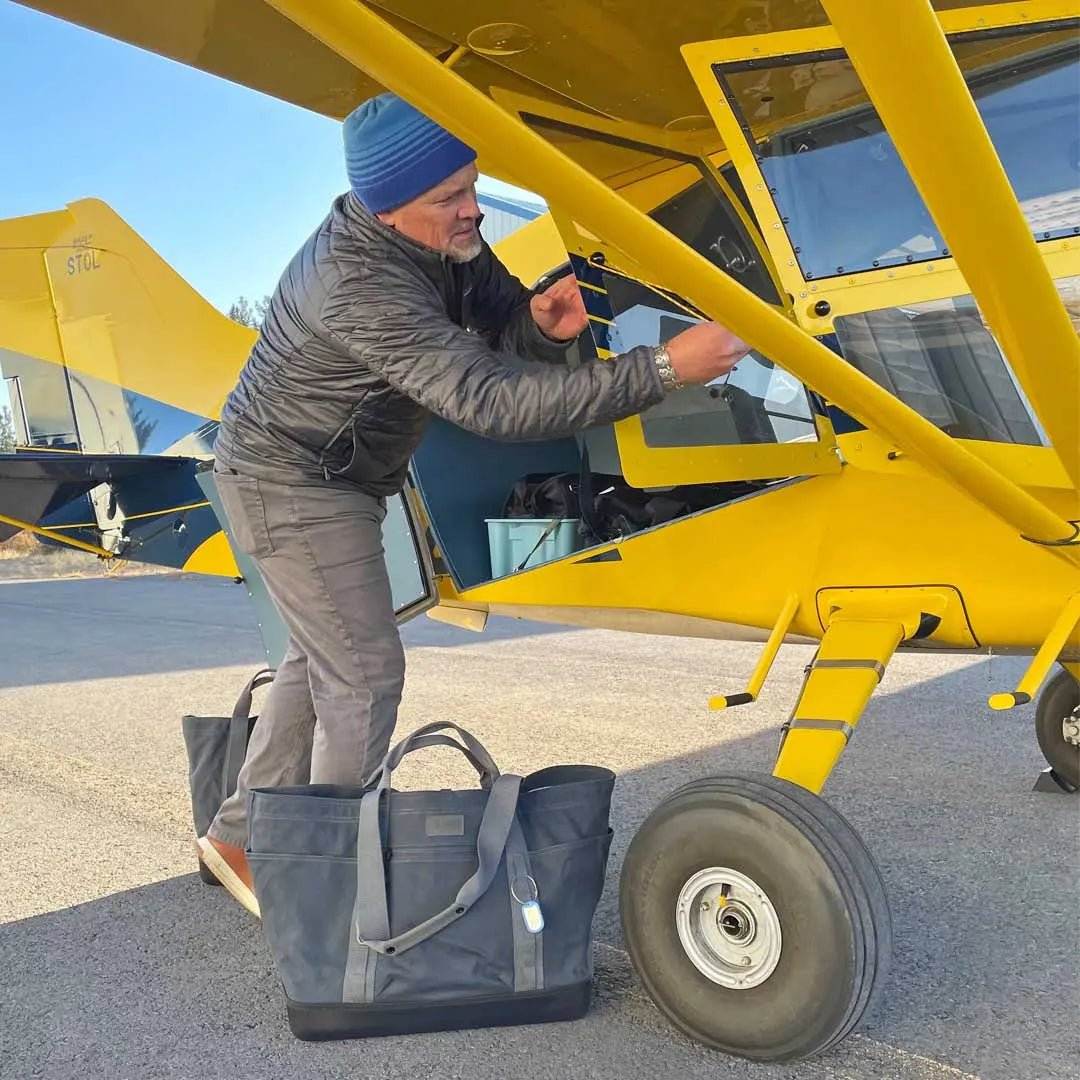Large Gear Tote used by a man beside a yellow plane, showcasing its durability and versatility.