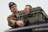 Man securing green 95L Rugged Case on vehicle roof rack outdoors
