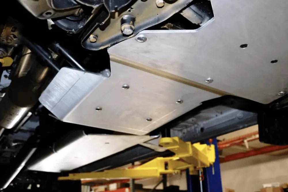 Underbody view of a 4x4 Sprinter fitted with a 1/4" thick aluminum transmission and transfer case skid plate for drivetrain protection.